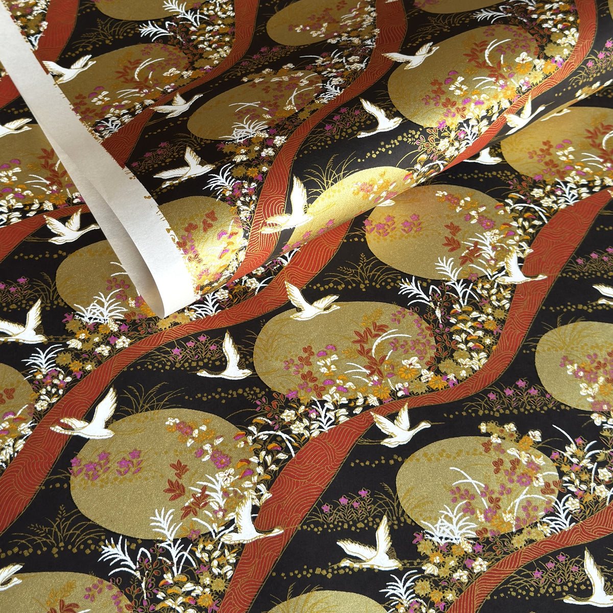 a sheet of Japanese yuzen chiyogami paper in white cranes, flowers and rivers in muted tones of autumn colours and lots of gold on a black ground.