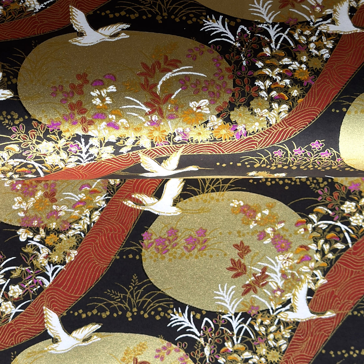 a sheet of Japanese yuzen chiyogami paper in white cranes, flowers and rivers in muted tones of autumn colours and lots of gold on a black ground.