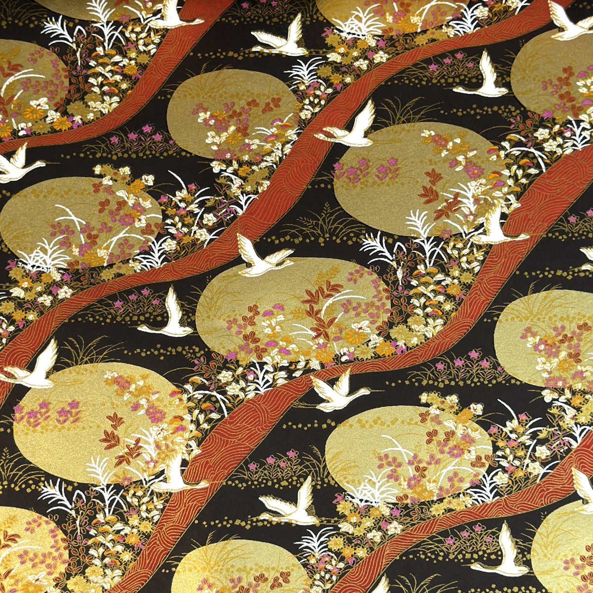 a sheet of Japanese yuzen chiyogami paper in white cranes, flowers and rivers in muted tones of autumn colours and lots of gold on a black ground.