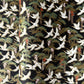 A close-up of a sheet of Japanese chiyogami paper featuring white cranes flying over green pine trees and branches on a black background.