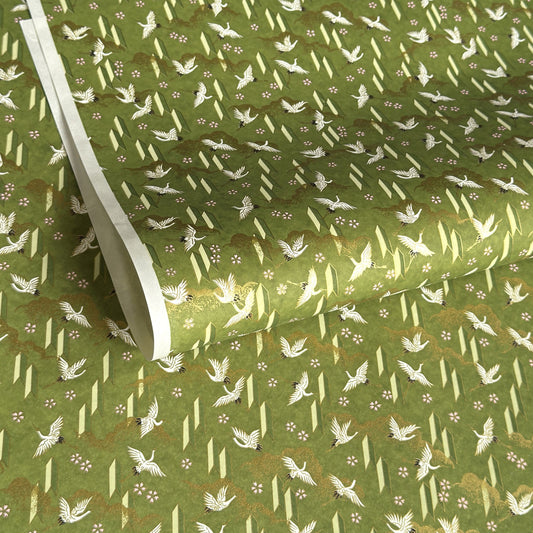 a sheet of Japanese chiyogami paper with an olive green ground and a pattern of white flying cranes and arrows.  There are also little pink cherry blossom flowers and gold clouds.