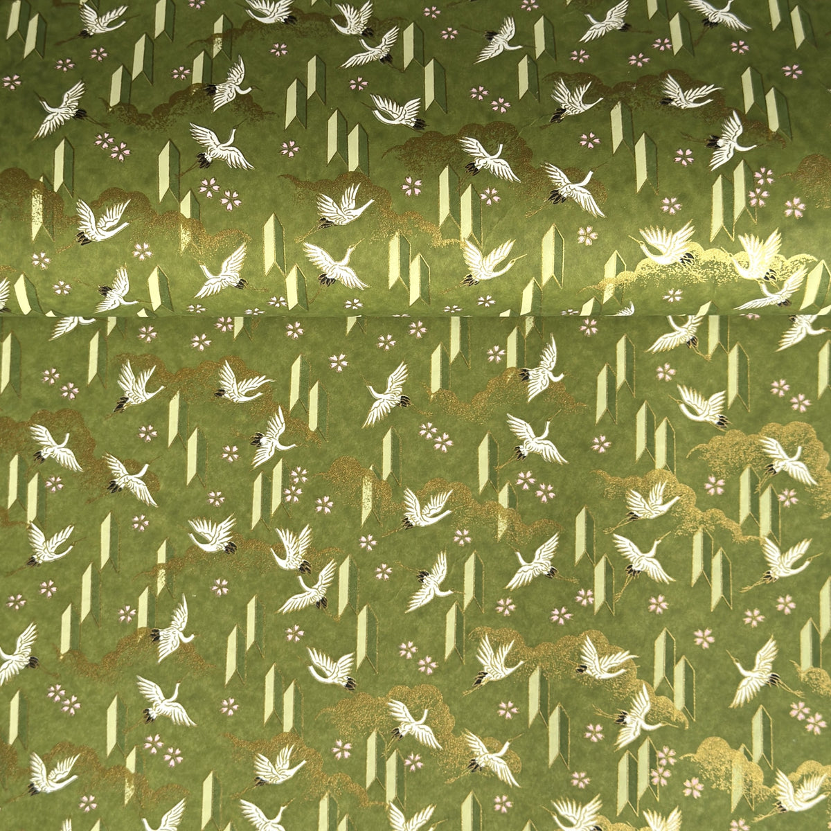 a sheet of Japanese chiyogami paper with an olive green ground and a pattern of white flying cranes and arrows.  There are also little pink cherry blossom flowers and gold clouds.