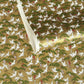 A close-up of a sheet of Japanese chiyogami paper with a repeating Japanese-style pattern featuring white cranes, green pine trees, and small red floral accents on a gold background.