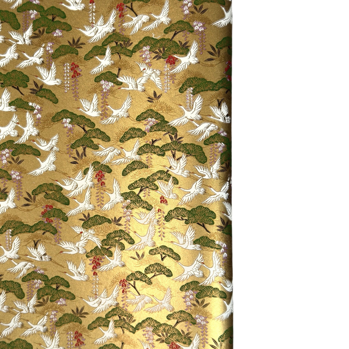 A close-up of a sheet of Japanese chiyogami paper with a repeating Japanese-style pattern featuring white cranes, green pine trees, and small red floral accents on a gold background.