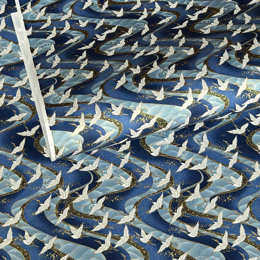 a sheet of Japanese Chiyogami paper with a hand screen printed pattern of white cranes in flight. The backdrop is swirling lines of dark and light blue with gold accents.