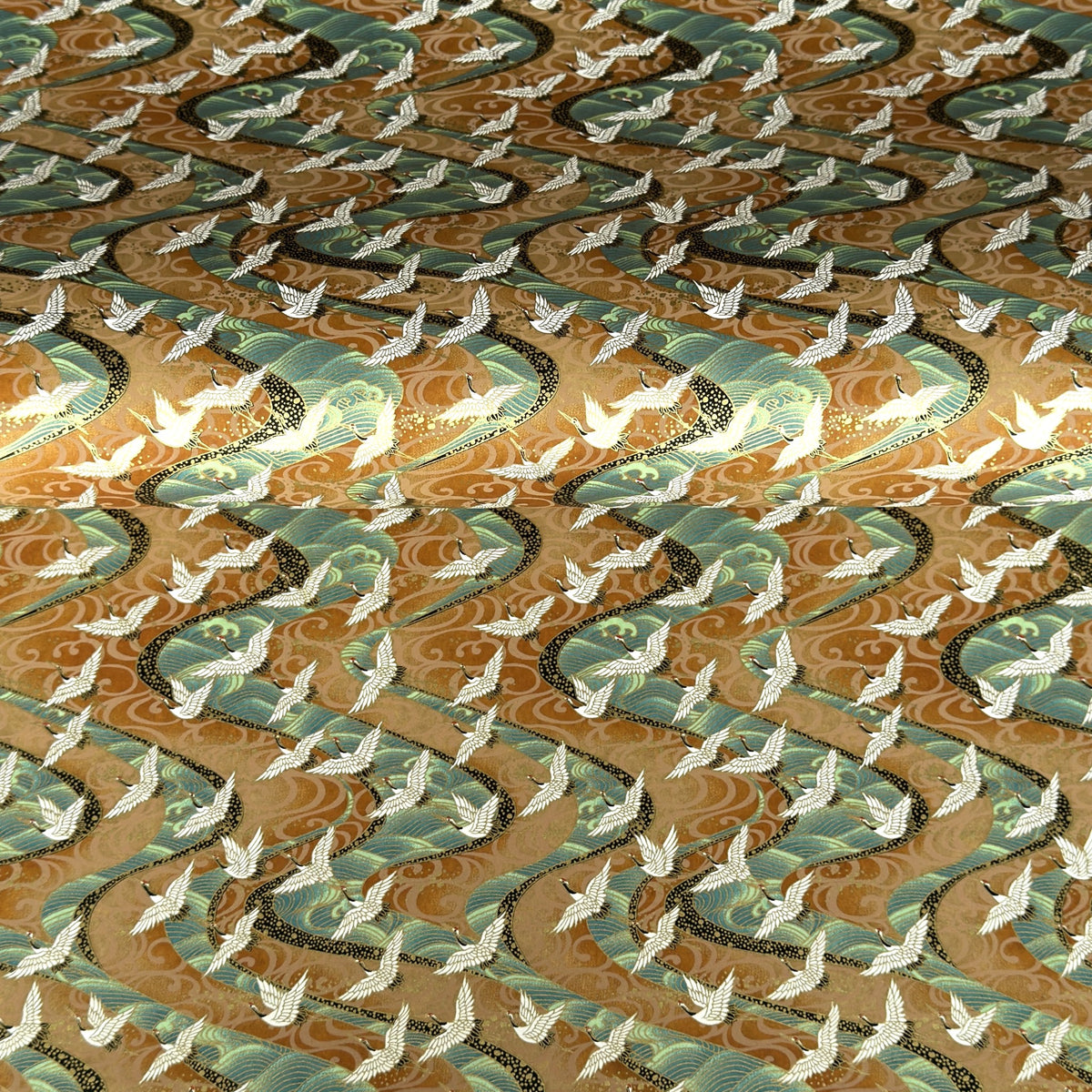 a sheet of Japanese chiyogami yuzen paper screen printed with a pattern of white flying cranes on a background of aqua and tan swirling lines