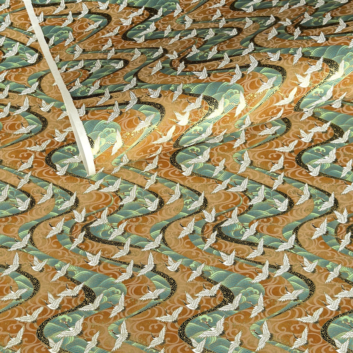 a sheet of Japanese chiyogami yuzen paper screen printed with a pattern of white flying cranes on a background of aqua and tan swirling lines