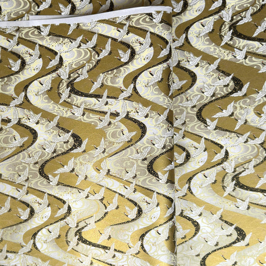 a sheet of Japanese chiyogami paper hand screen printed with a pattern of white cranes in flight.  The back drop is silver and lack swirling lines on gold. 