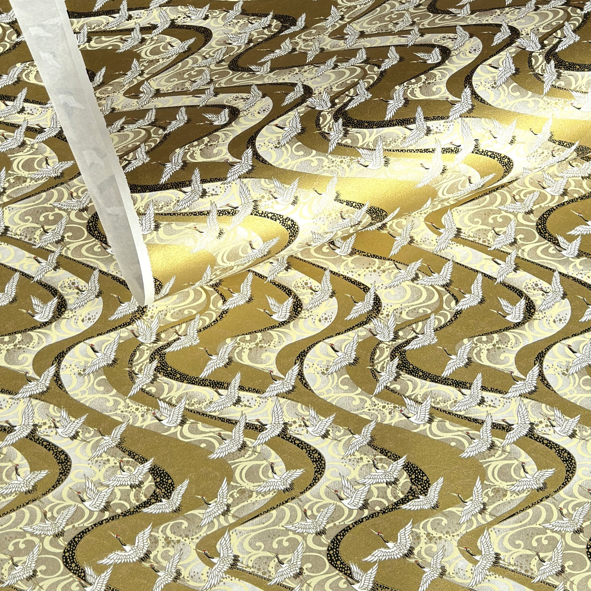 a sheet of Japanese chiyogami paper hand screen printed with a pattern of white cranes in flight.  The back drop is silver and lack swirling lines on gold. 