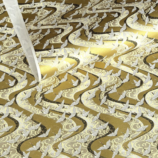a sheet of Japanese chiyogami paper hand screen printed with a pattern of white cranes in flight.  The back drop is silver and lack swirling lines on gold. 