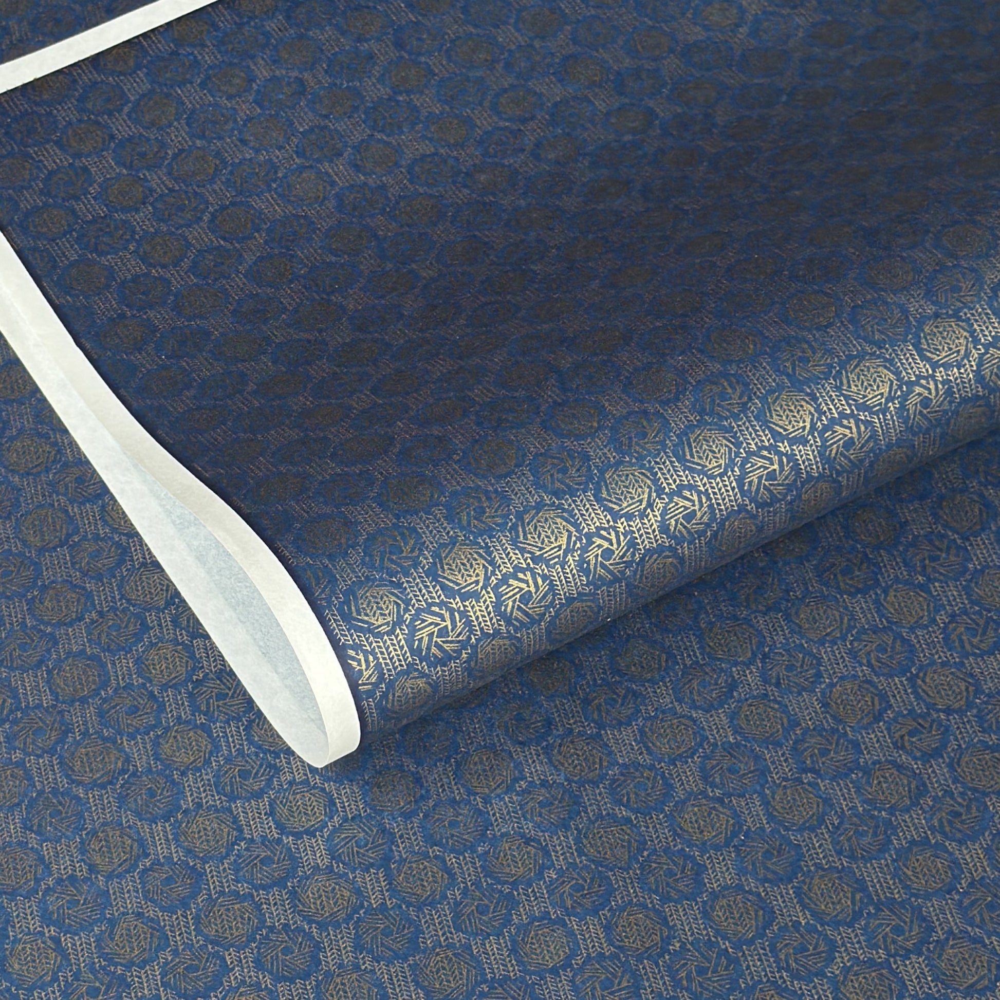 A sheet of Japanese chiyogami paper with a small repeat pattern of gold circular crests on a dark blue background.