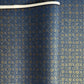 A sheet of Japanese chiyogami paper with a small repeat pattern of gold circular crests on a dark blue background.