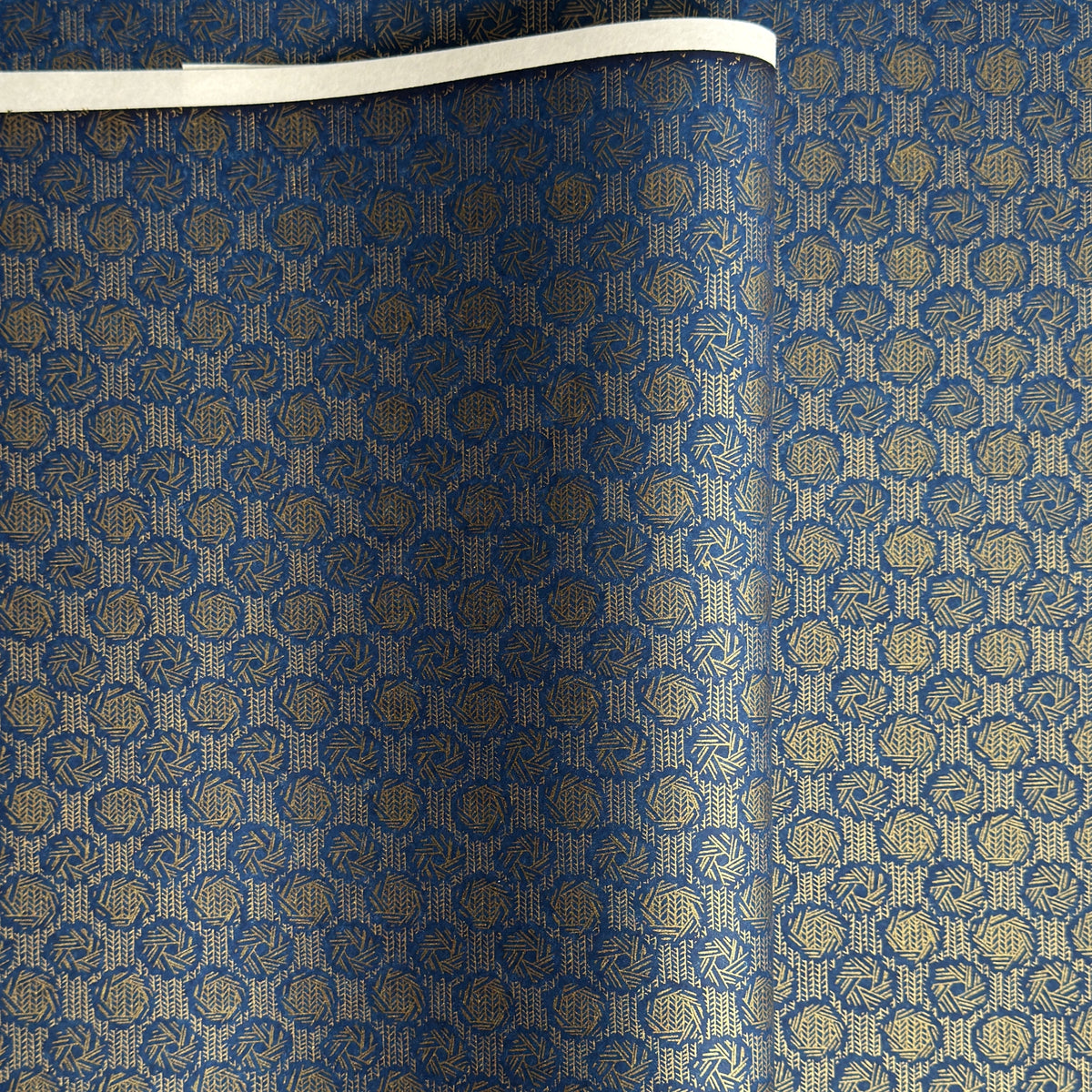 A sheet of Japanese chiyogami paper with a small repeat pattern of gold circular crests on a dark blue background.