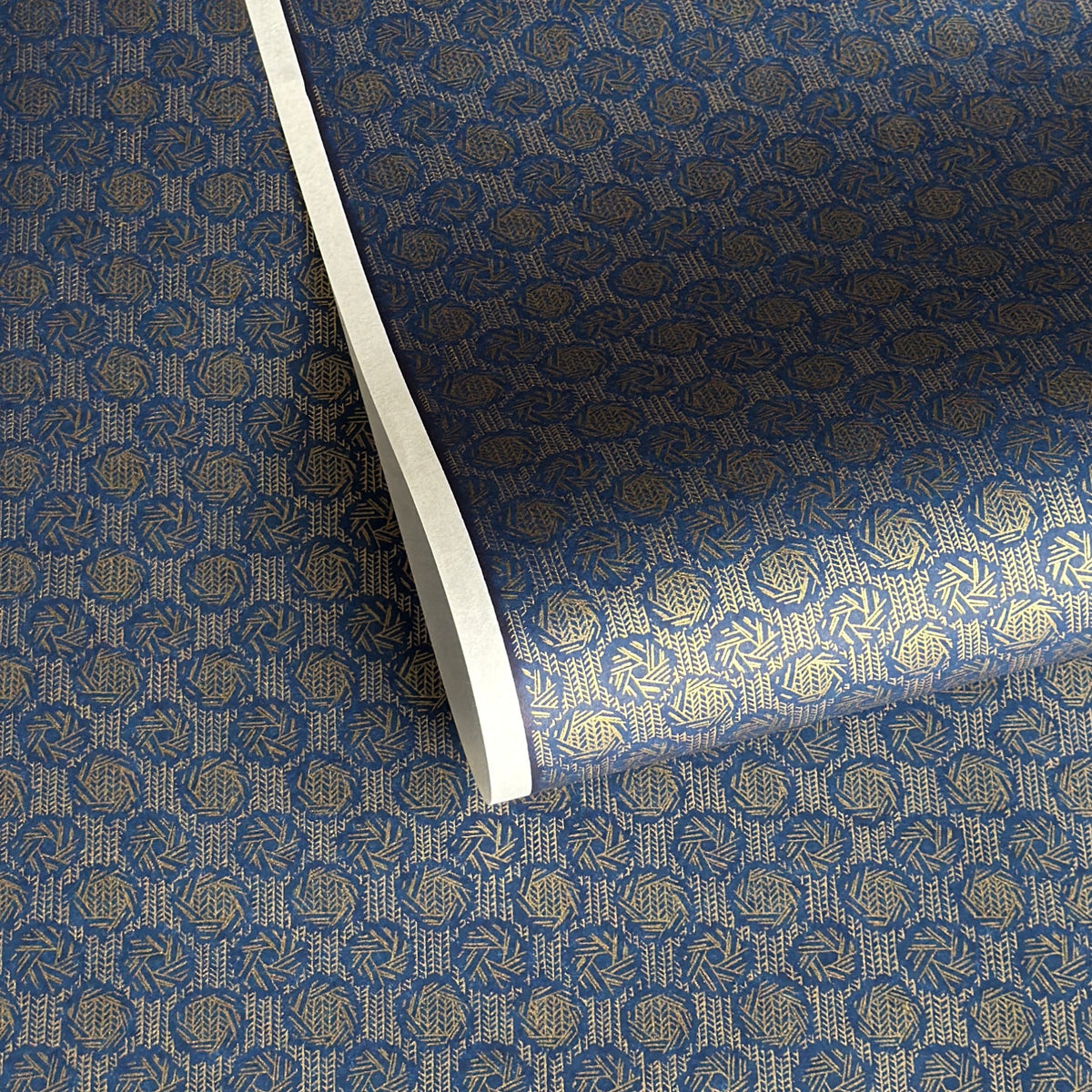 A sheet of Japanese chiyogami paper with a small repeat pattern of gold circular crests on a dark blue background.