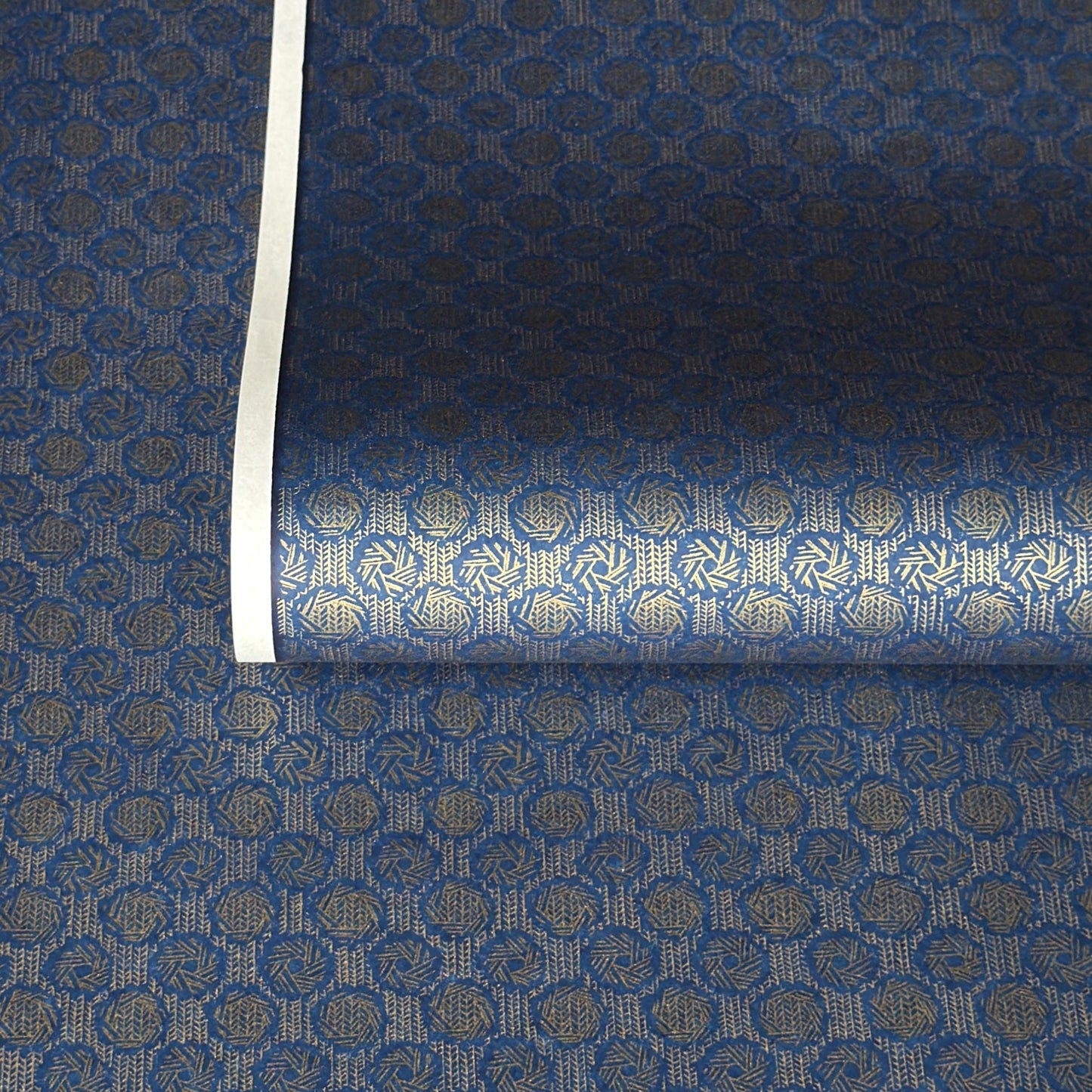 A sheet of Japanese chiyogami paper with a small repeat pattern of gold circular crests on a dark blue background.