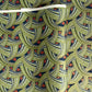 A close-up of a sheet of Japanese chiyogami paper with repeating curved wave-like motifs in olive green, navy blue, white, and small orange-red accents. 
