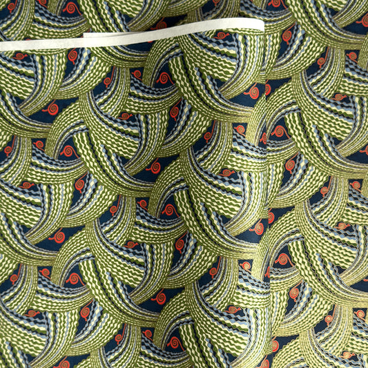 A close-up of a sheet of Japanese chiyogami paper with repeating curved wave-like motifs in olive green, navy blue, white, and small orange-red accents. 