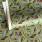 A close-up of a sheet of Japanese chiyogami paper with repeating curved wave-like motifs in olive green, navy blue, white, and small orange-red accents. 