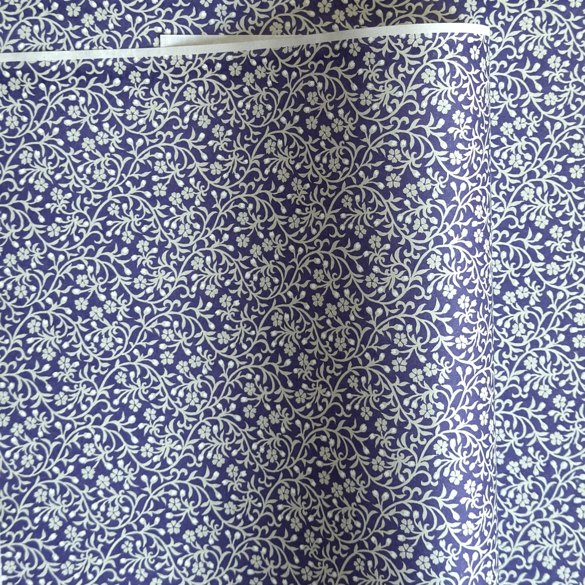 a sheet of Japanese silkscreen printed chiyogami paper with a small floral repeat pattern in grey and white on a periwinkle blue background