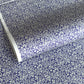 a sheet of Japanese silkscreen printed chiyogami paper with a small floral repeat pattern in grey and white on a periwinkle blue background