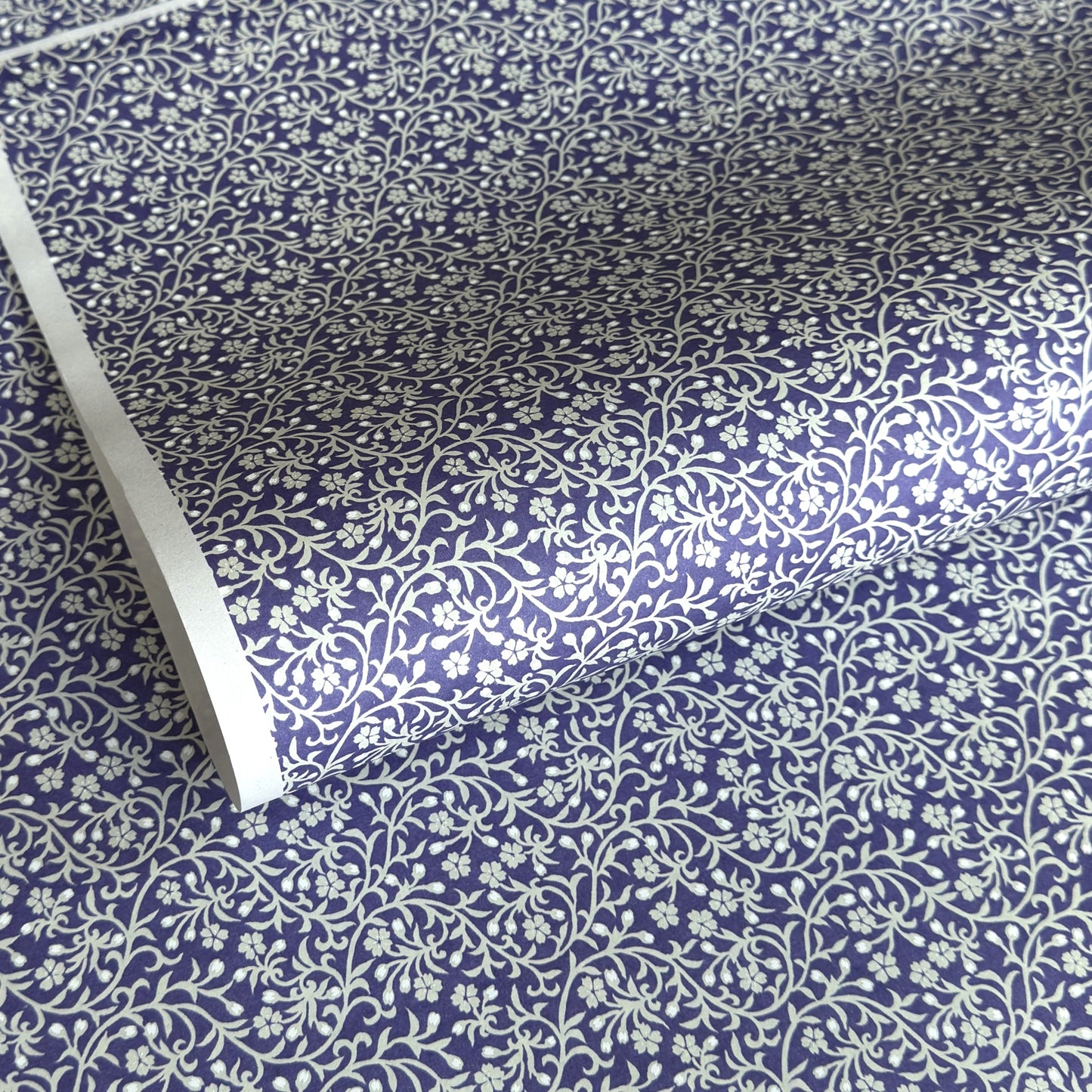 a sheet of Japanese silkscreen printed chiyogami paper with a small floral repeat pattern in grey and white on a periwinkle blue background