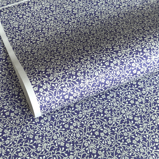 a sheet of Japanese silkscreen printed chiyogami paper with a small floral repeat pattern in grey and white on a periwinkle blue background