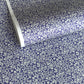 a sheet of Japanese silkscreen printed chiyogami paper with a small floral repeat pattern in grey and white on a periwinkle blue background
