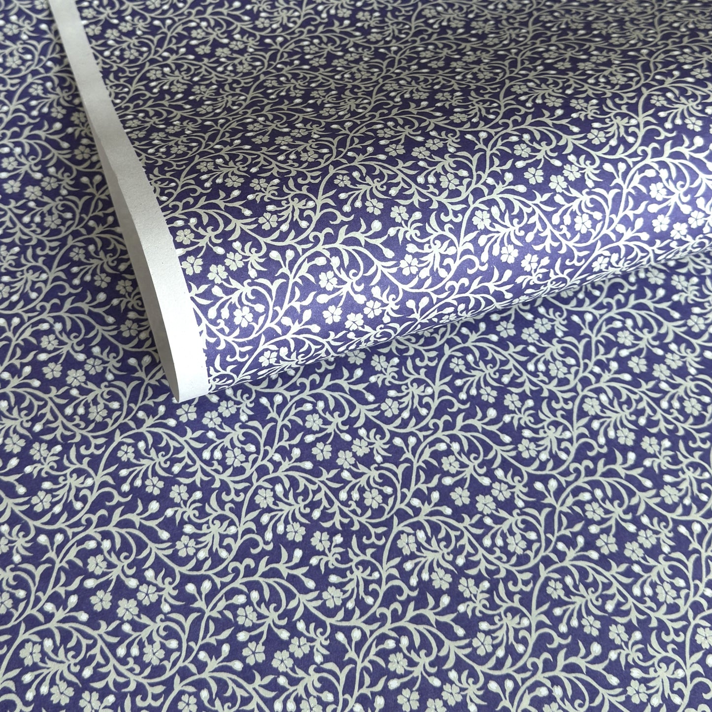 a sheet of Japanese silkscreen printed chiyogami paper with a small floral repeat pattern in grey and white on a periwinkle blue background