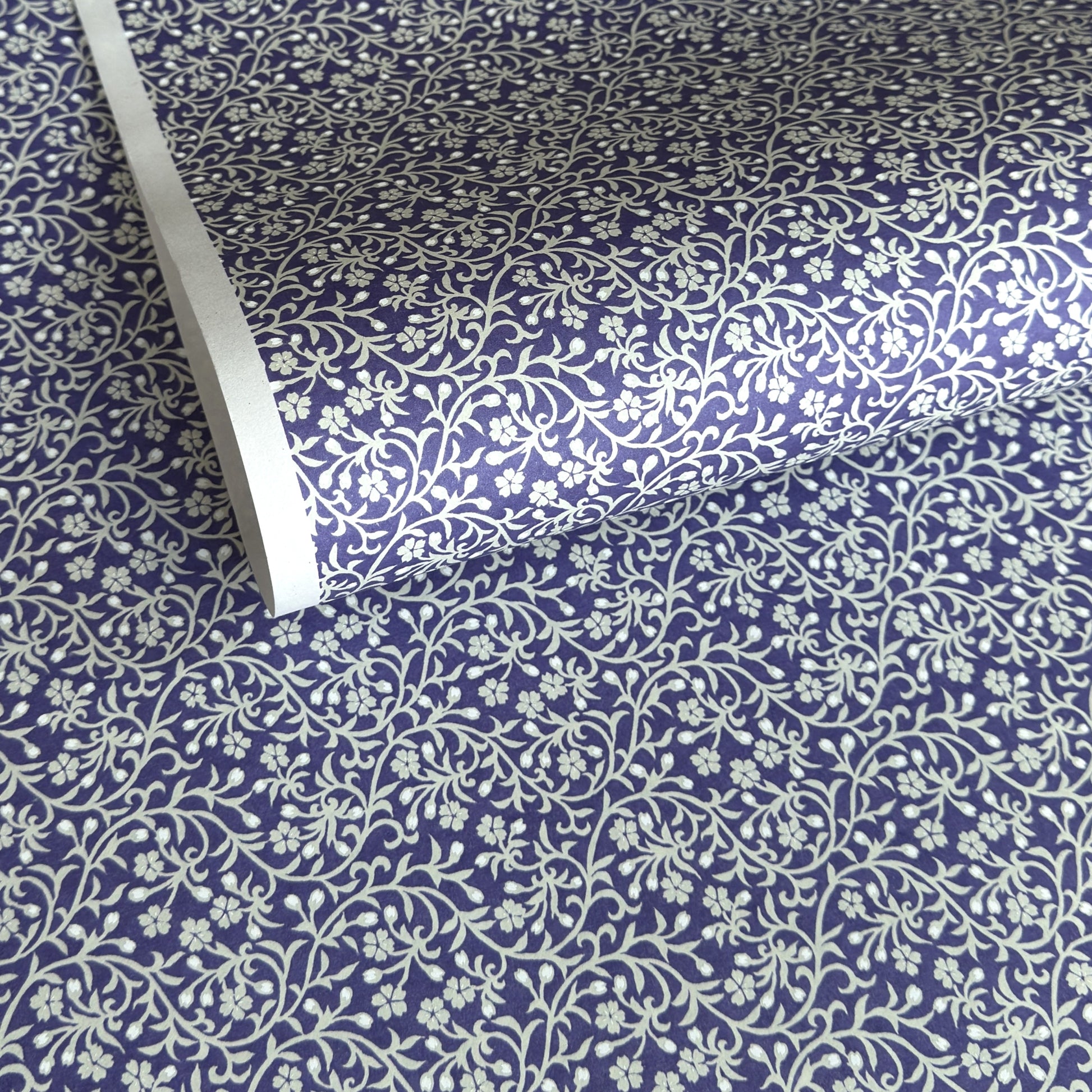 a sheet of Japanese silkscreen printed chiyogami paper with a small floral repeat pattern in grey and white on a periwinkle blue background