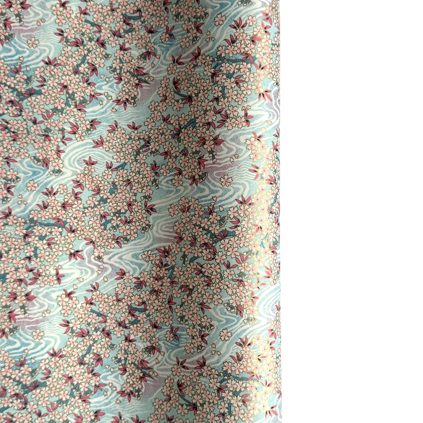 Japanese silkscreen chiyogami paper with an abundance of pale pink cherry blossom with a pale blue backdrop of meandering water, finished with metallic gold ink.