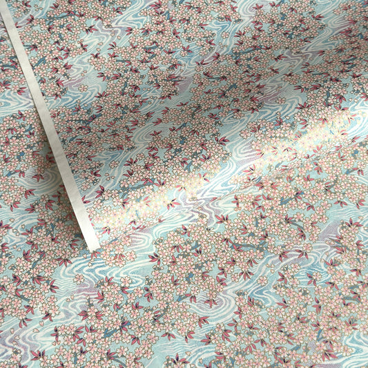 Japanese silkscreen chiyogami paper with an abundance of pale pink cherry blossom with a pale blue backdrop of meandering water, finished with metallic gold ink.
