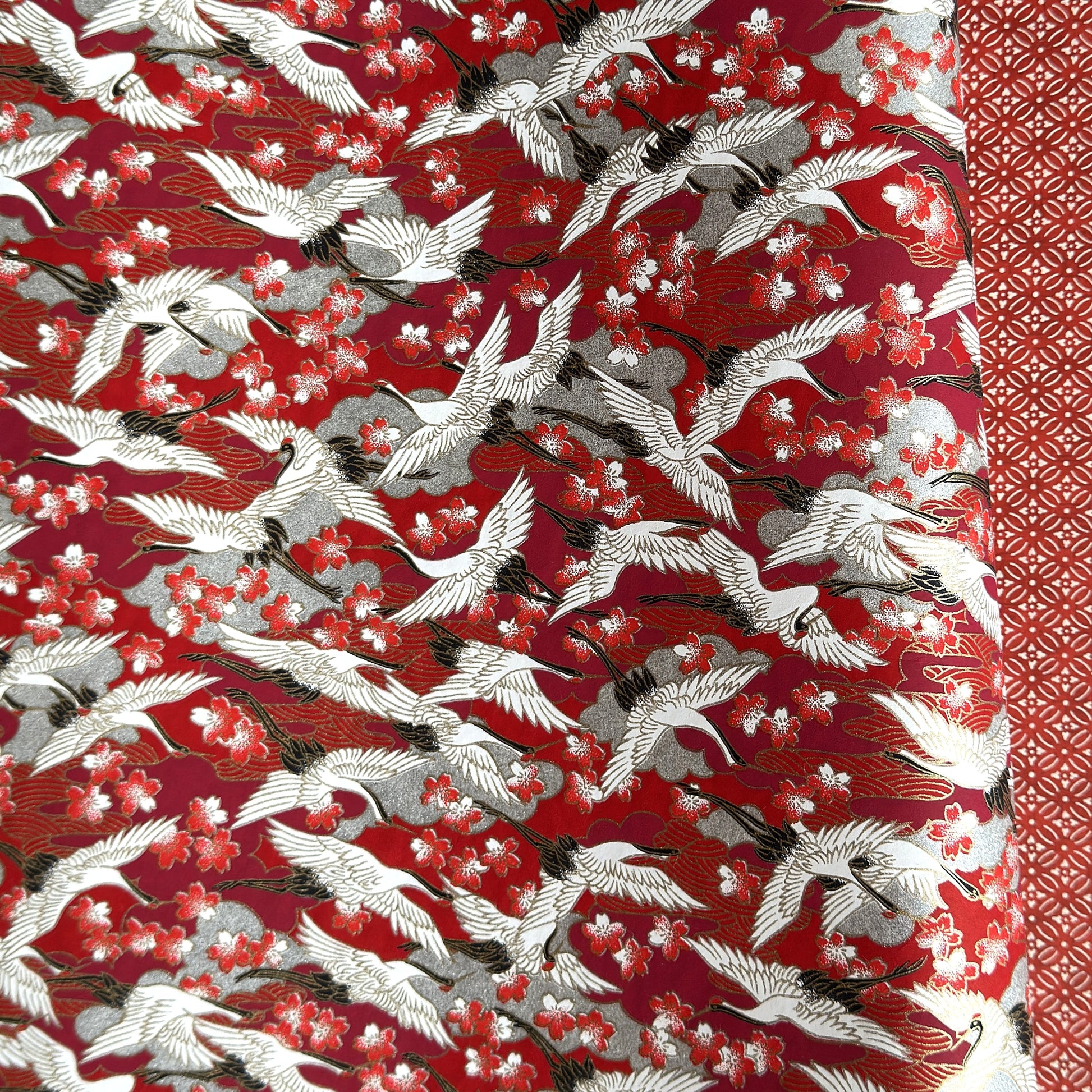 Japanese silkscreen chiyogami paper with a repeat pattern of white cranes in flight on a red and silver background