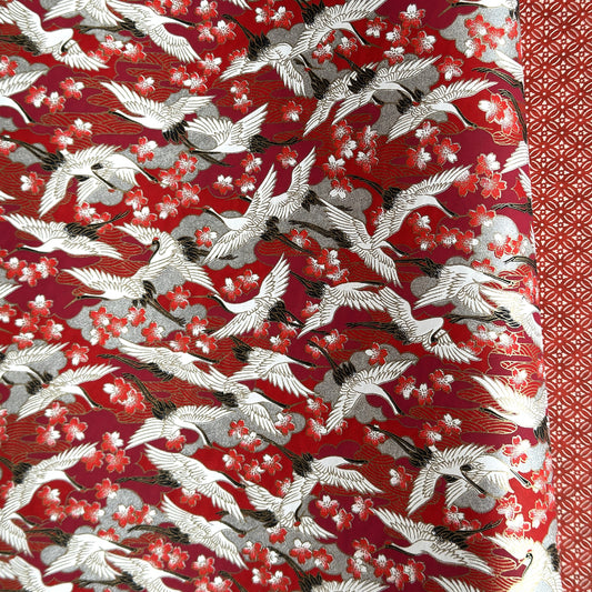 Japanese silkscreen chiyogami paper with a repeat pattern of white cranes in flight on a red and silver background