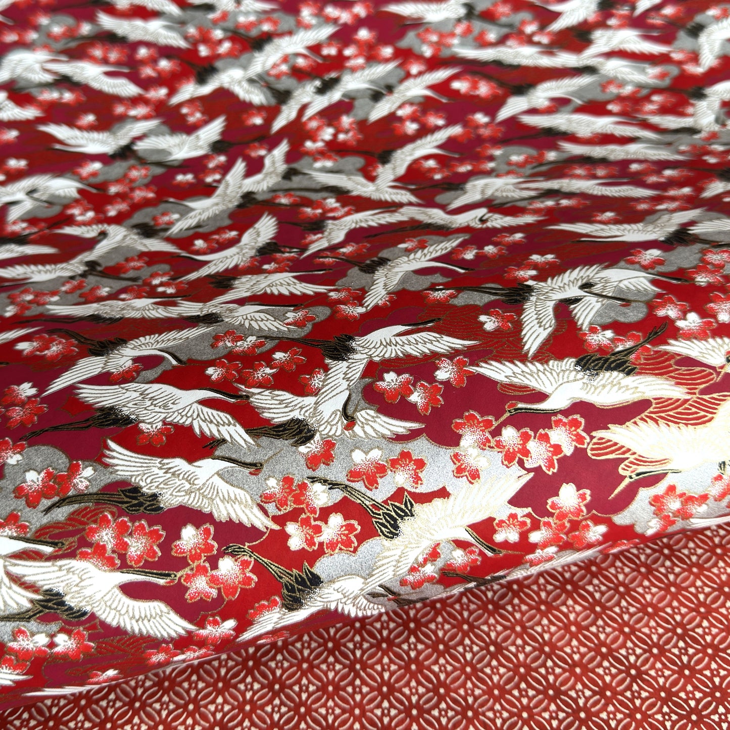 Japanese silkscreen chiyogami paper with a repeat pattern of white cranes in flight on a red and silver background