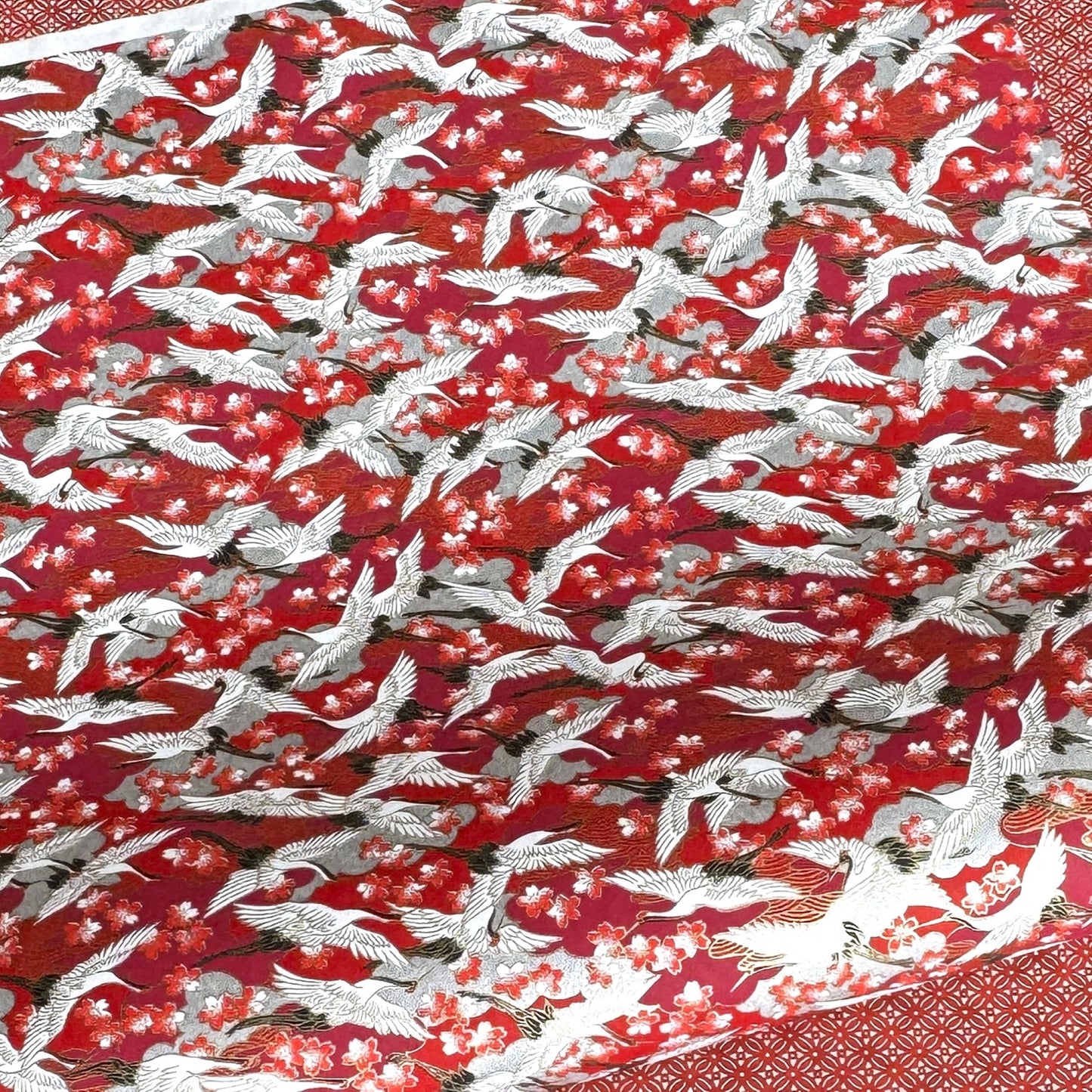 Japanese silkscreen chiyogami paper with a repeat pattern of white cranes in flight on a red and silver background