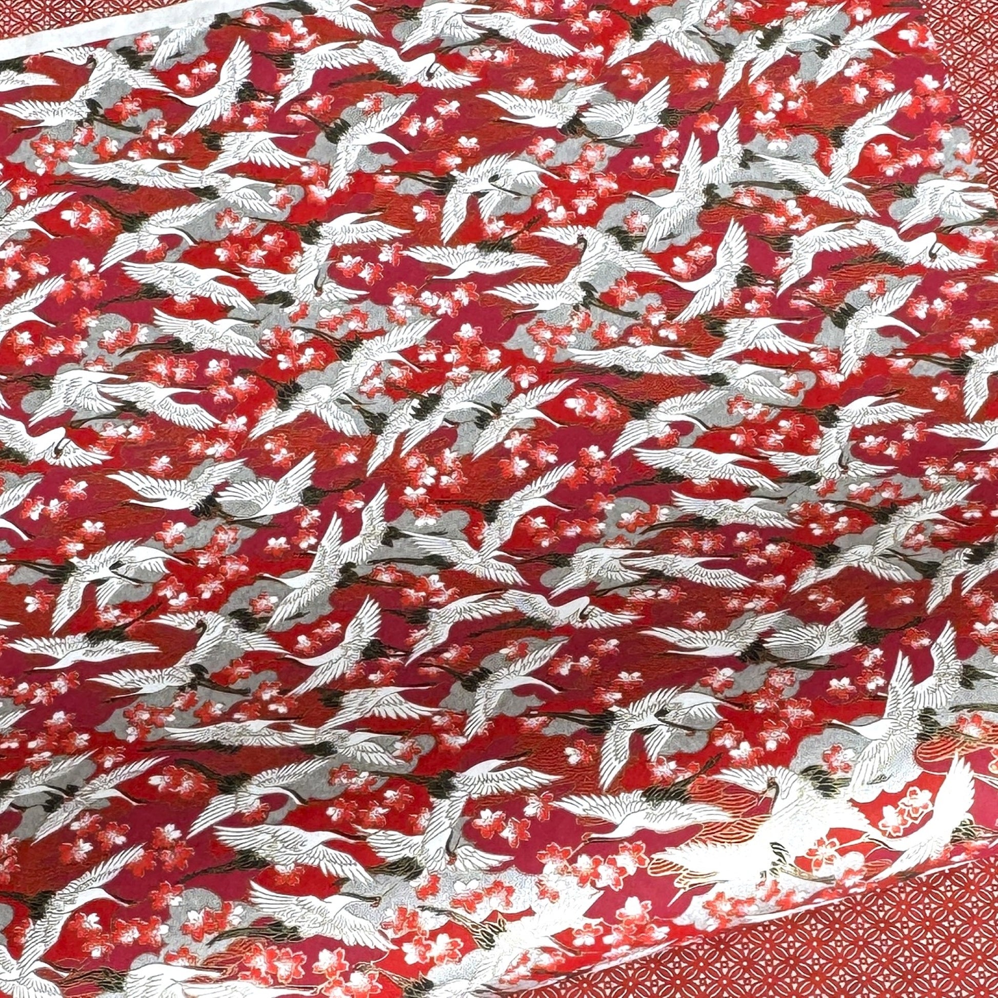 Japanese silkscreen chiyogami paper with a repeat pattern of white cranes in flight on a red and silver background