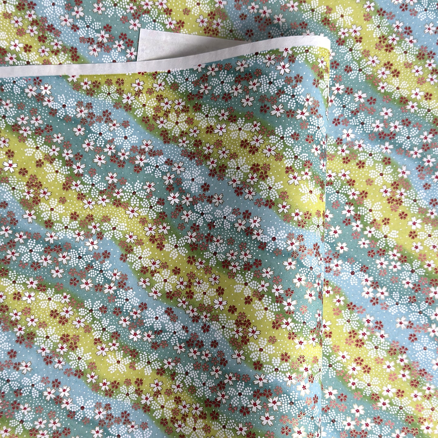 Japanese chiyogami paper silkscreened with a dainty pattern of white sakura flowers on an backdrop of aqua and lime diagonal wavy stripes