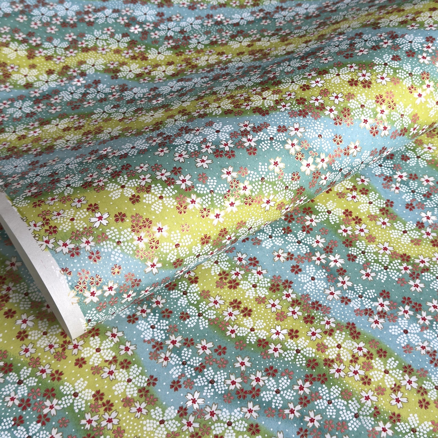 Japanese chiyogami paper silkscreened with a dainty pattern of white sakura flowers on an backdrop of aqua and lime diagonal wavy stripes
