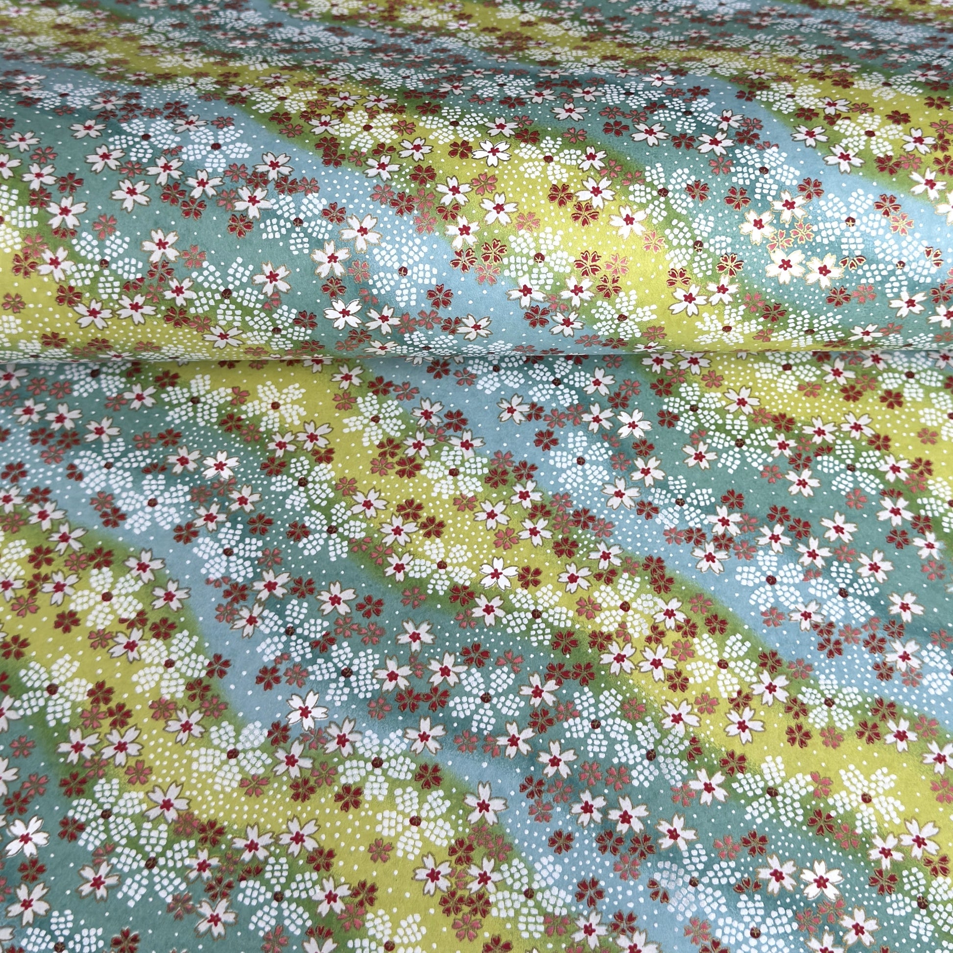 Japanese chiyogami paper silkscreened with a dainty pattern of white sakura flowers on an backdrop of aqua and lime diagonal wavy stripes