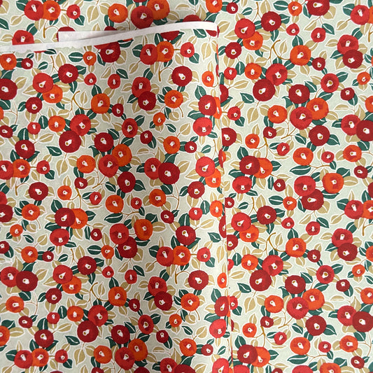 Japanese silkscreen chiyogami paper with a repeat pattern of camellia flowers in red and orange on a soft green ground