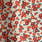 Japanese silkscreen chiyogami paper with a repeat pattern of camellia flowers in red and orange on a soft green ground
