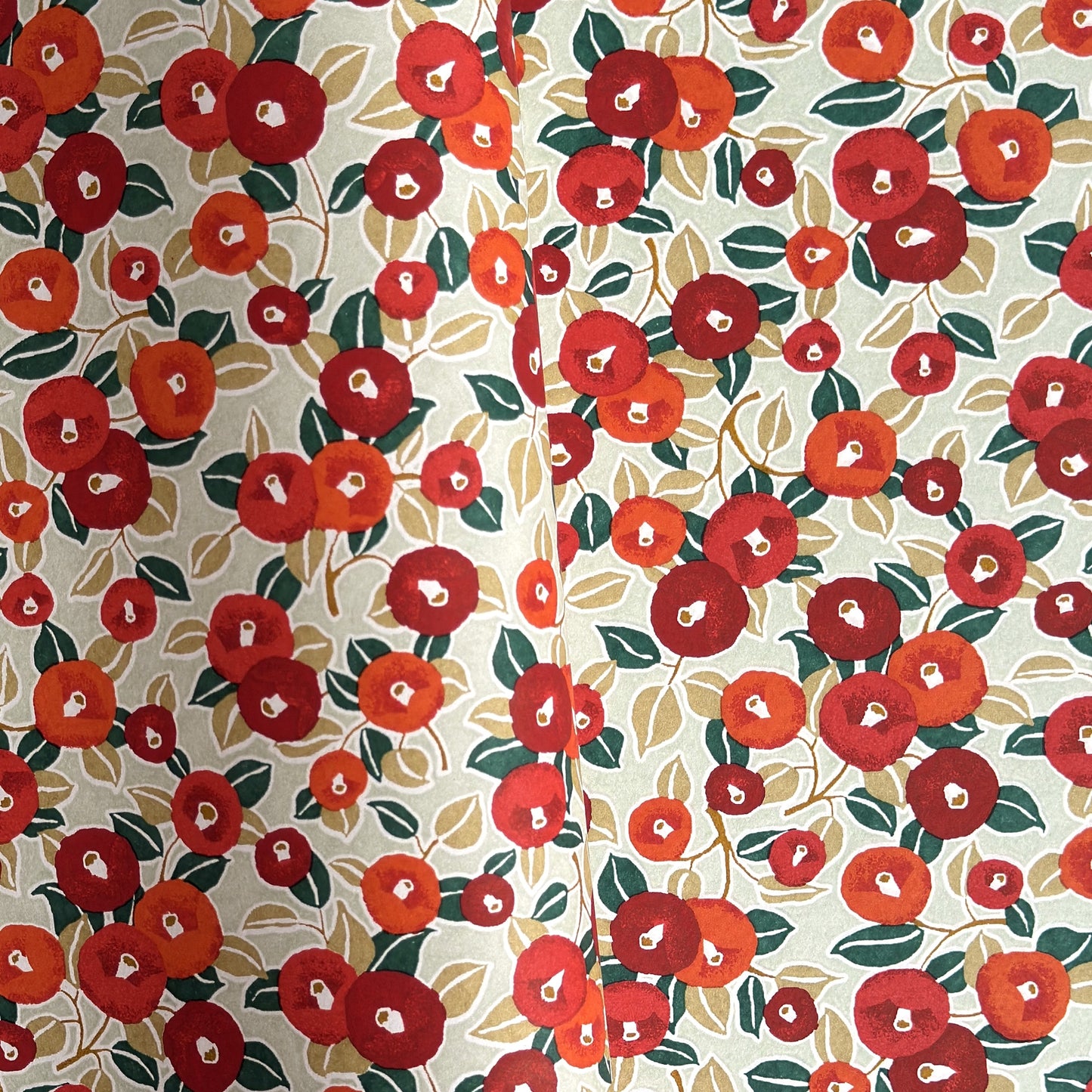 Japanese silkscreen chiyogami paper with a repeat pattern of camellia flowers in red and orange on a soft green ground