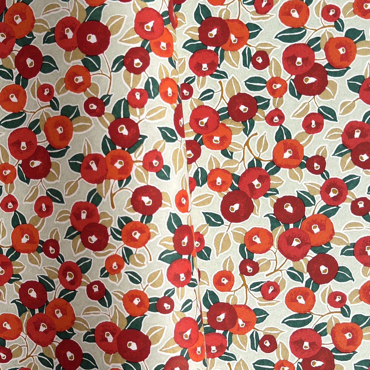 Japanese silkscreen chiyogami paper with a repeat pattern of camellia flowers in red and orange on a soft green ground