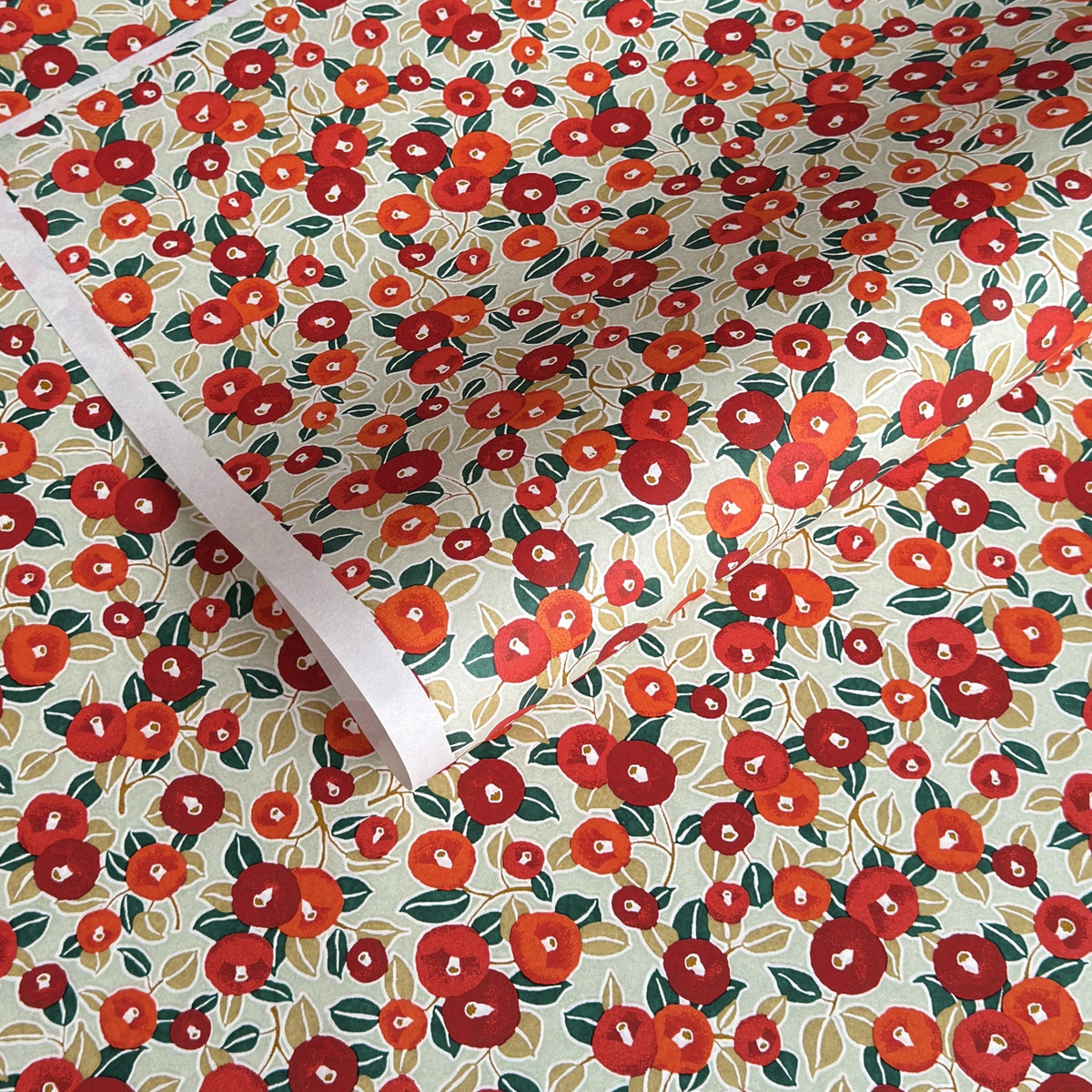 Japanese silkscreen chiyogami paper with a repeat pattern of camellia flowers in red and orange on a soft green ground