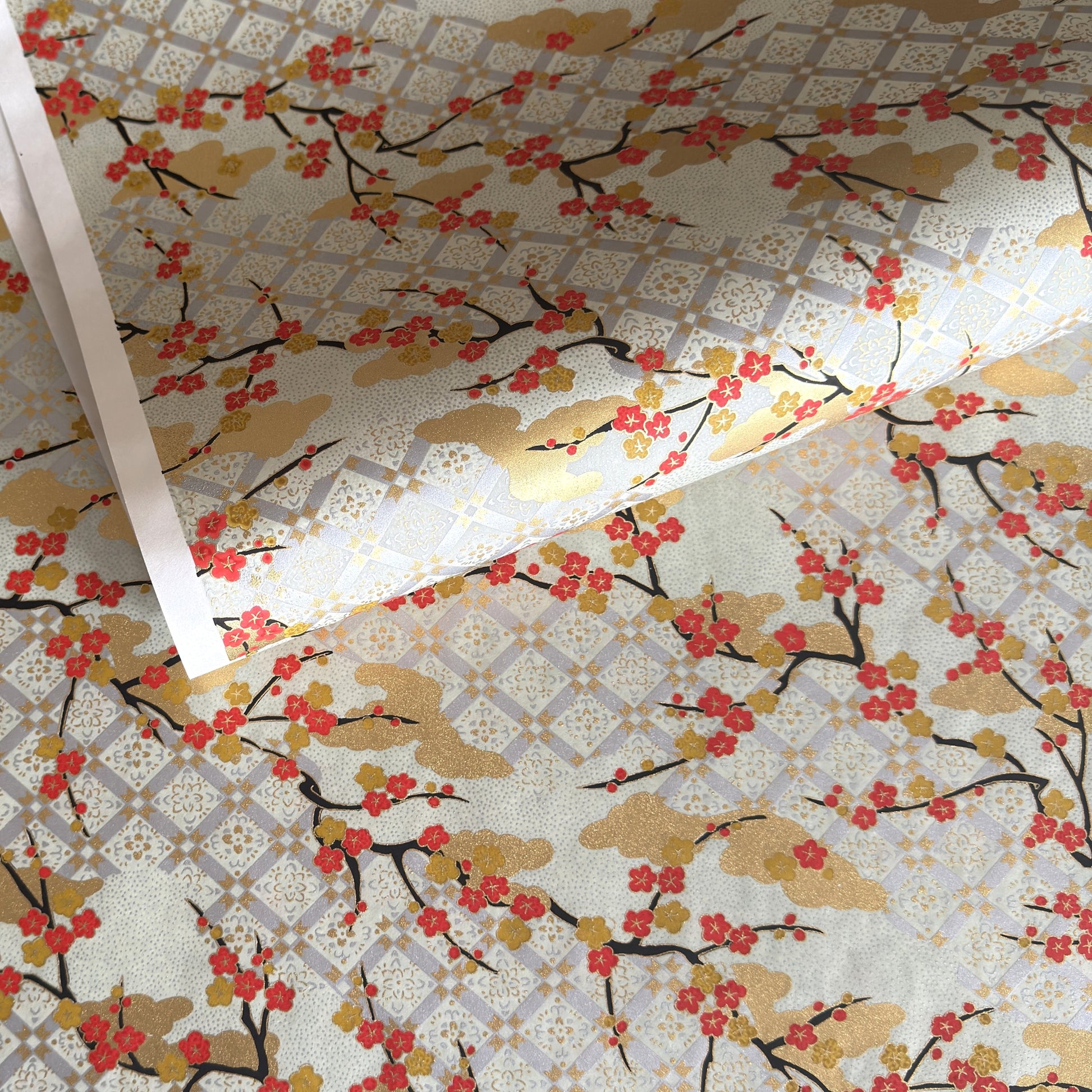 japanese silk-screen handmade paper, chiyogami, showing branches of red cherry blossom and gold clouds on a backdrop of silver, cream and gold