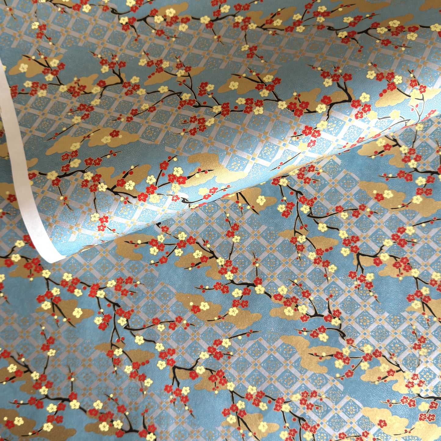japanese silk-screen handmade paper showing branches of red blossom, gold clouds on a teal, gold and silver geometric backdrop.