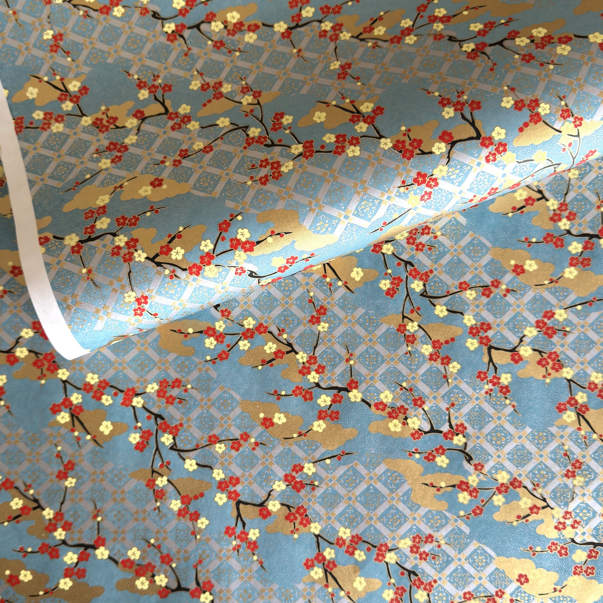 japanese silk-screen handmade paper showing branches of red blossom, gold clouds on a teal, gold and silver geometric backdrop.