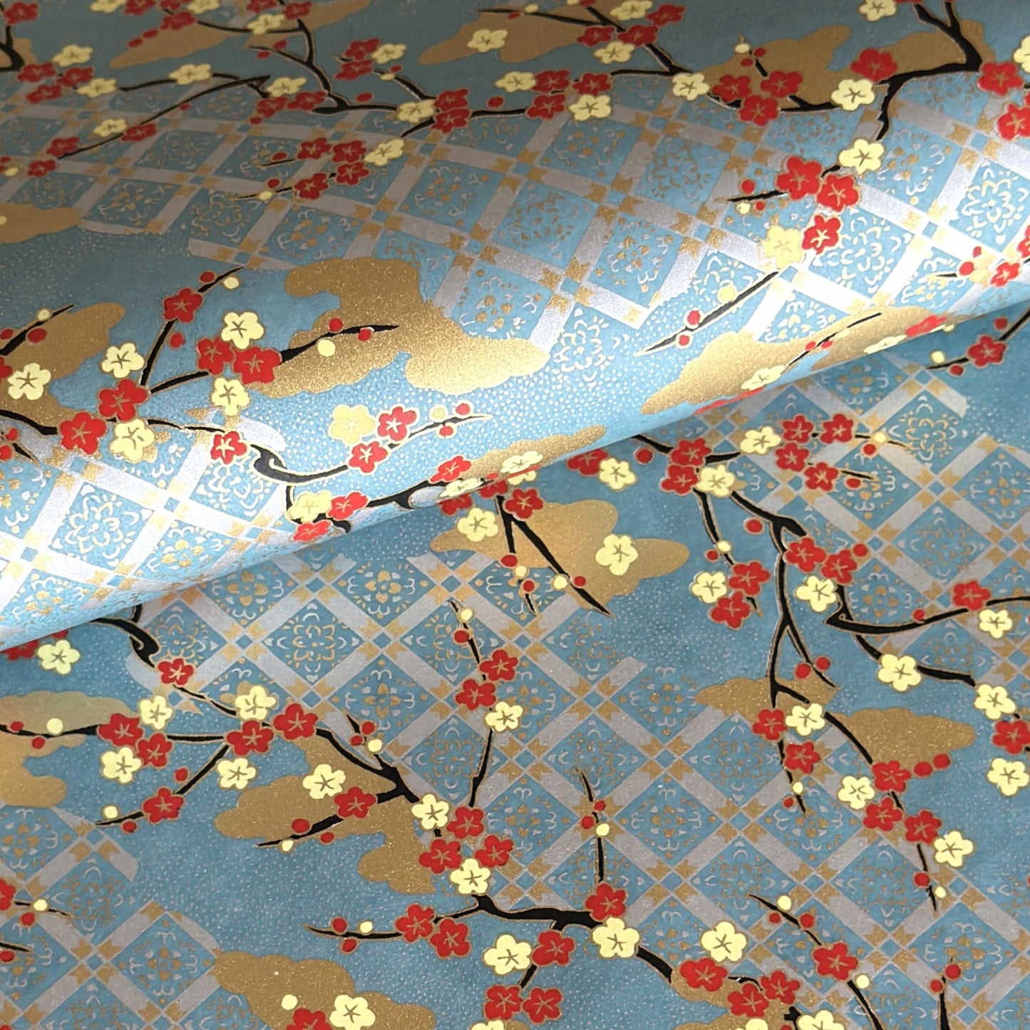 japanese silk-screen handmade paper showing branches of red blossom, gold clouds on a teal, gold and silver geometric backdrop.