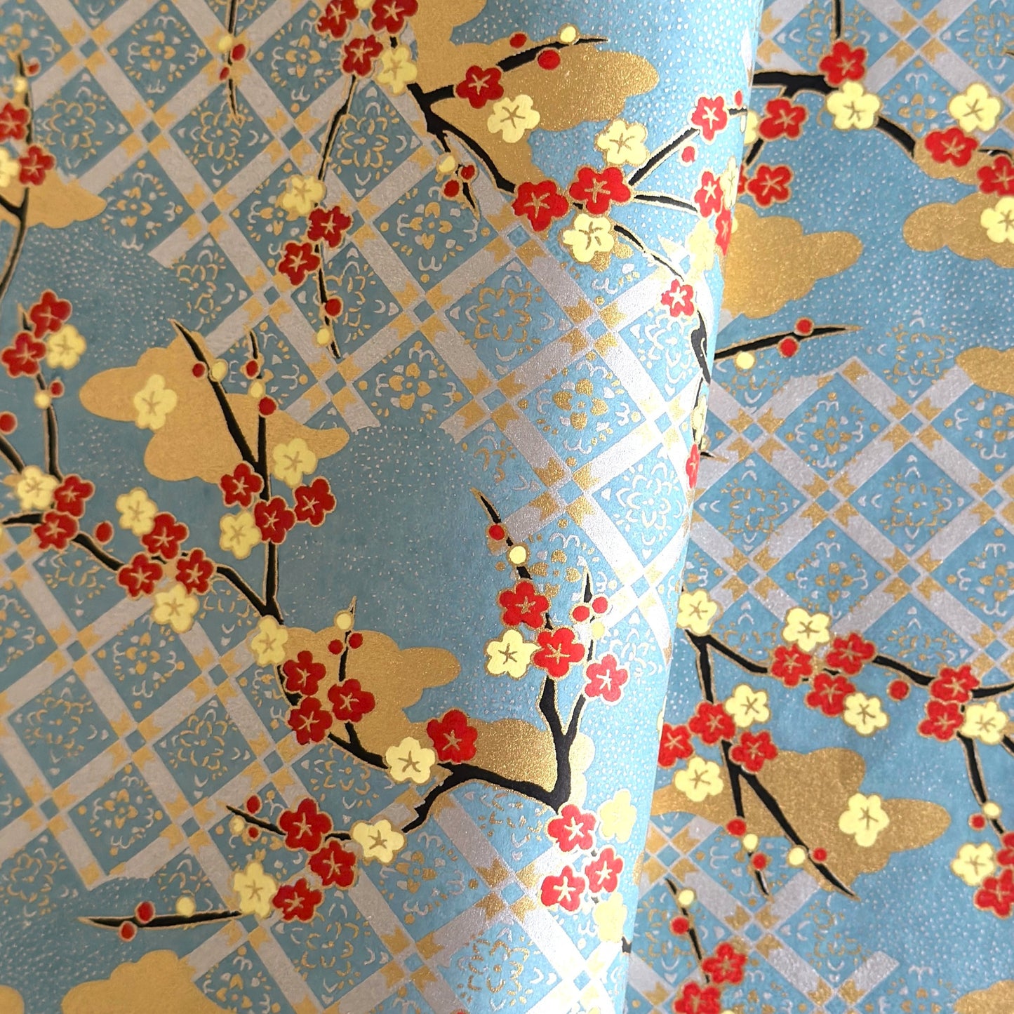 japanese silk-screen handmade paper showing branches of red blossom, gold clouds on a teal, gold and silver geometric backdrop.