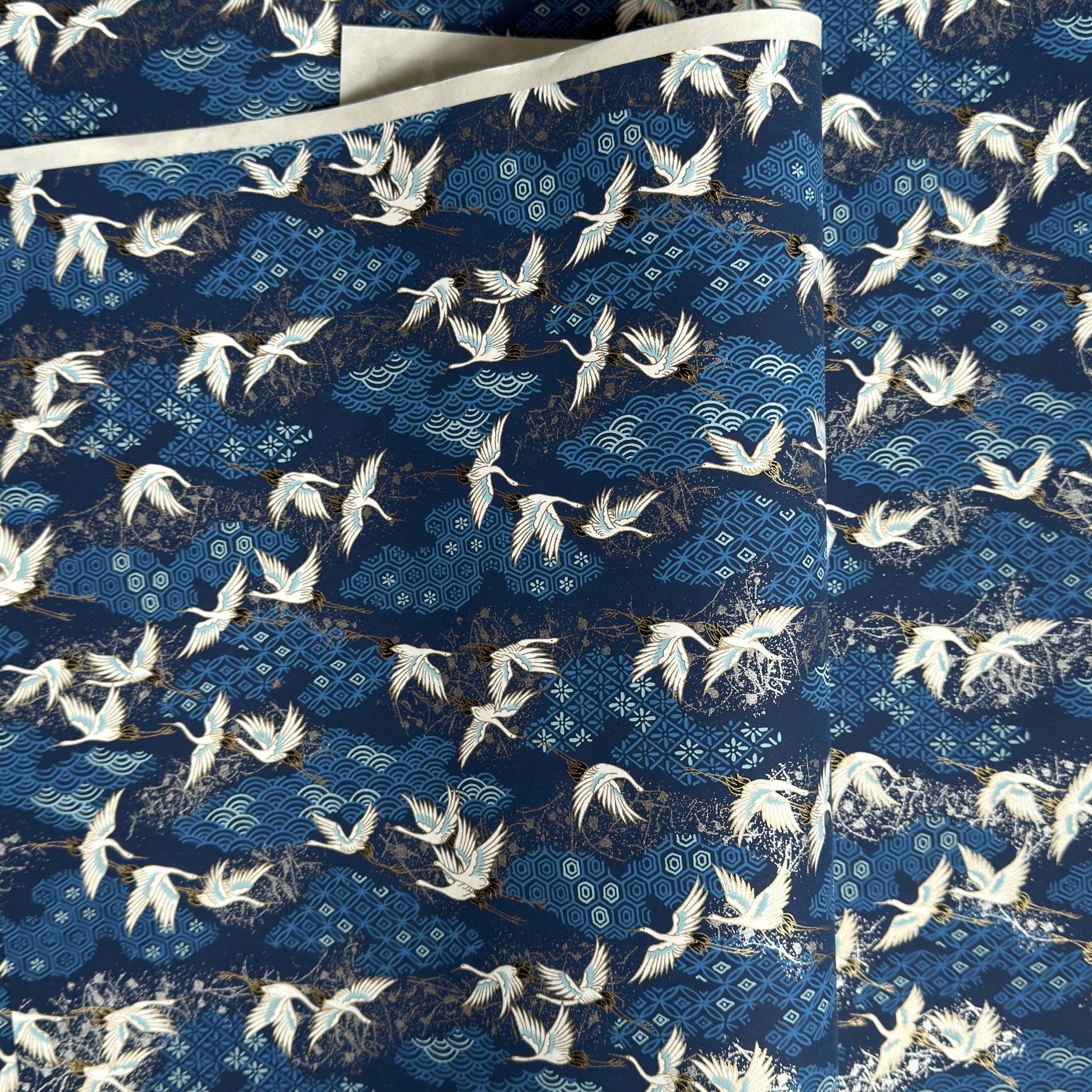 a sheet of Japanese chiyogami yuzen paper with a traditional pattern of white cranes flying with a deep blue background of patterned clouds
